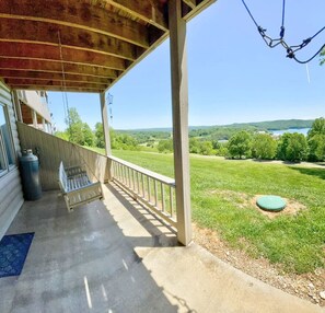 A covered porch with a swing, a view of a grassy field, and a body of water in the distance. - 2C Condo: Lake/Ridge/Golf Views (LaFollette)
