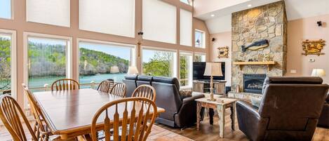 A spacious room with a large dining table, comfortable seating, a fireplace, and a scenic view of a lake.