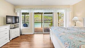 Een slaapkamer met een televisie, een bed, een dressoir en uitzicht op een balkon met een houten terras.