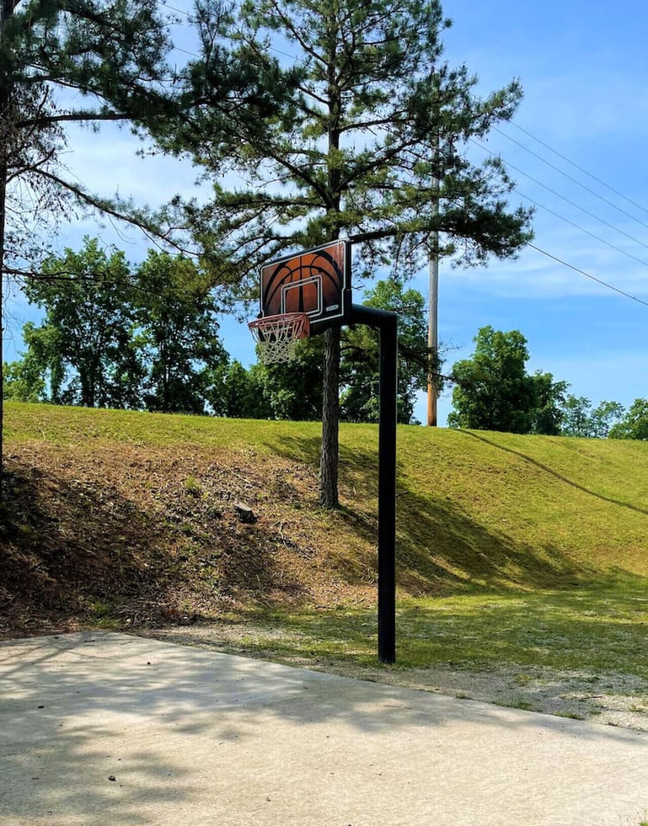 A basketball hoop with a backboard, set on a concrete surface with a grassy slope behind it.
