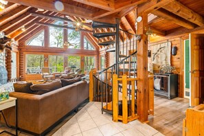A log cabin interior with a wooden staircase, a sofa, and a fireplace.