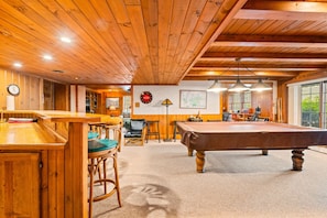 Un intérieur en bois comprenant une table de billard, un bar et un espace détente avec des sièges.