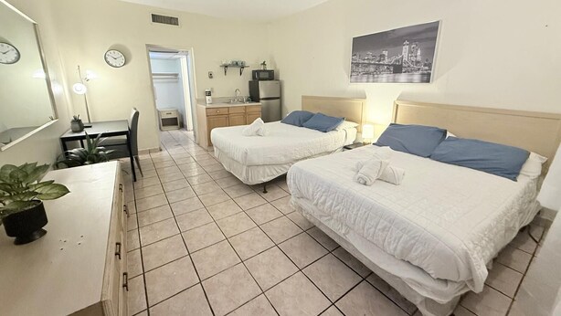 Une chambre d’hôtel avec deux lits, un bureau, une chaise, une petite kitchenette et une salle de bain.