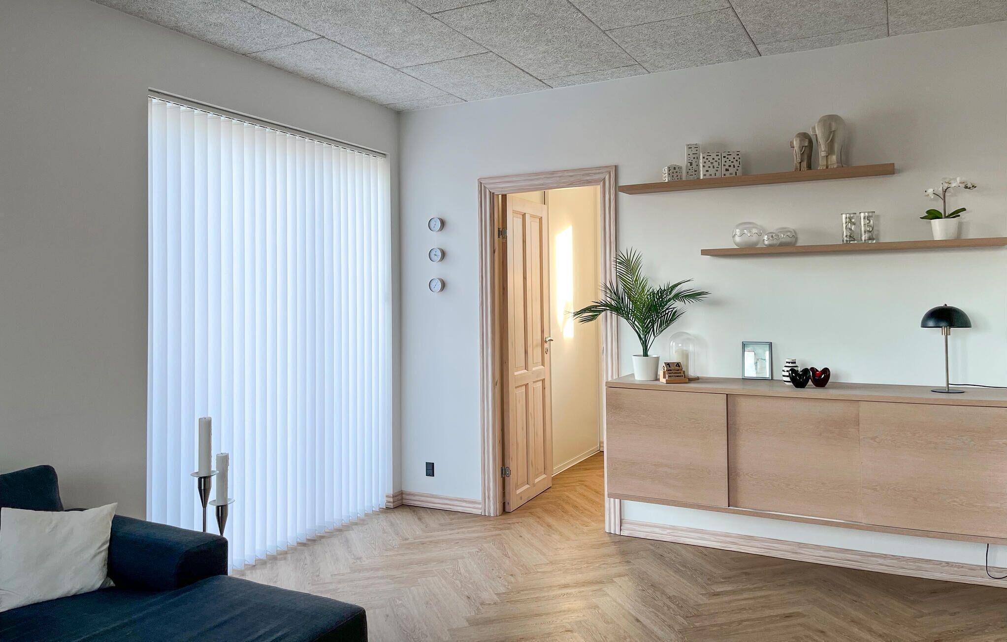 Ein modernes Wohnzimmer mit einem dunkelblauen Sofa, Holzboden und einer hellen Holzkommode mit Dekoration.