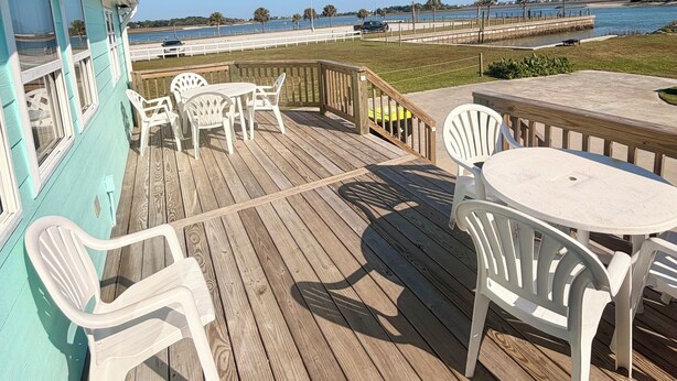 A wooden deck with outdoor seating, a view of the water, and a flag. - Water’s Edge at Randall’s - Cottage Overlooking the Intracoastal Waterway (Shallotte)