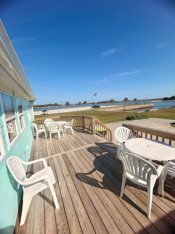 A wooden deck with outdoor seating, a view of the water, and a flag. - Water’s Edge at Randall’s - Cottage Overlooking the Intracoastal Waterway (Shallotte)