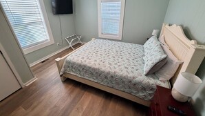A bedroom with a bed, a TV mounted on the wall, and two windows with blinds. - Water’s Edge at Randall’s - Cottage Overlooking the Intracoastal Waterway (Shallotte)