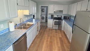 A kitchen with white cabinets, a dishwasher, a microwave, a stove, and a refrigerator. - Water’s Edge at Randall’s - Cottage Overlooking the Intracoastal Waterway (Shallotte)