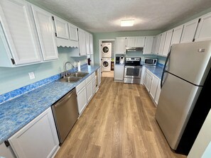 Eine Küche mit weißen Schränken, einem Geschirrspüler, einem Backofen mit zwei Garstufen, einer Mikrowelle und einem Kühlschrank.