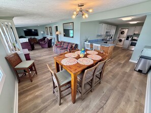 Uma sala de estar ampla com uma mesa de jantar de madeira, cadeiras e um sofá colorido.