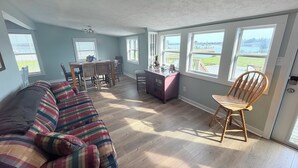A spacious room with a large window, a dining table, and a sofa. - Water’s Edge at Randall’s - Cottage Overlooking the Intracoastal Waterway (Shallotte)