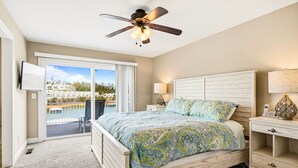 Een slaapkamer met een bed, een plafondventilator, een nachtkastje, een lamp en uitzicht op een waterpartij.