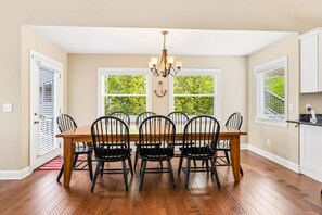 A dining room with a wooden table and chairs, a chandelier, and windows with greenery outside. - 112#4 Condo: Modern, Lakefront, Spacious (LaFollette)