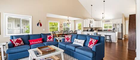 A spacious living room with a blue sectional sofa, a coffee table, and a kitchen in the background.
