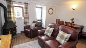 A living room with a fireplace, leather sofas, plaid curtains, a dining table, and a wooden floor.