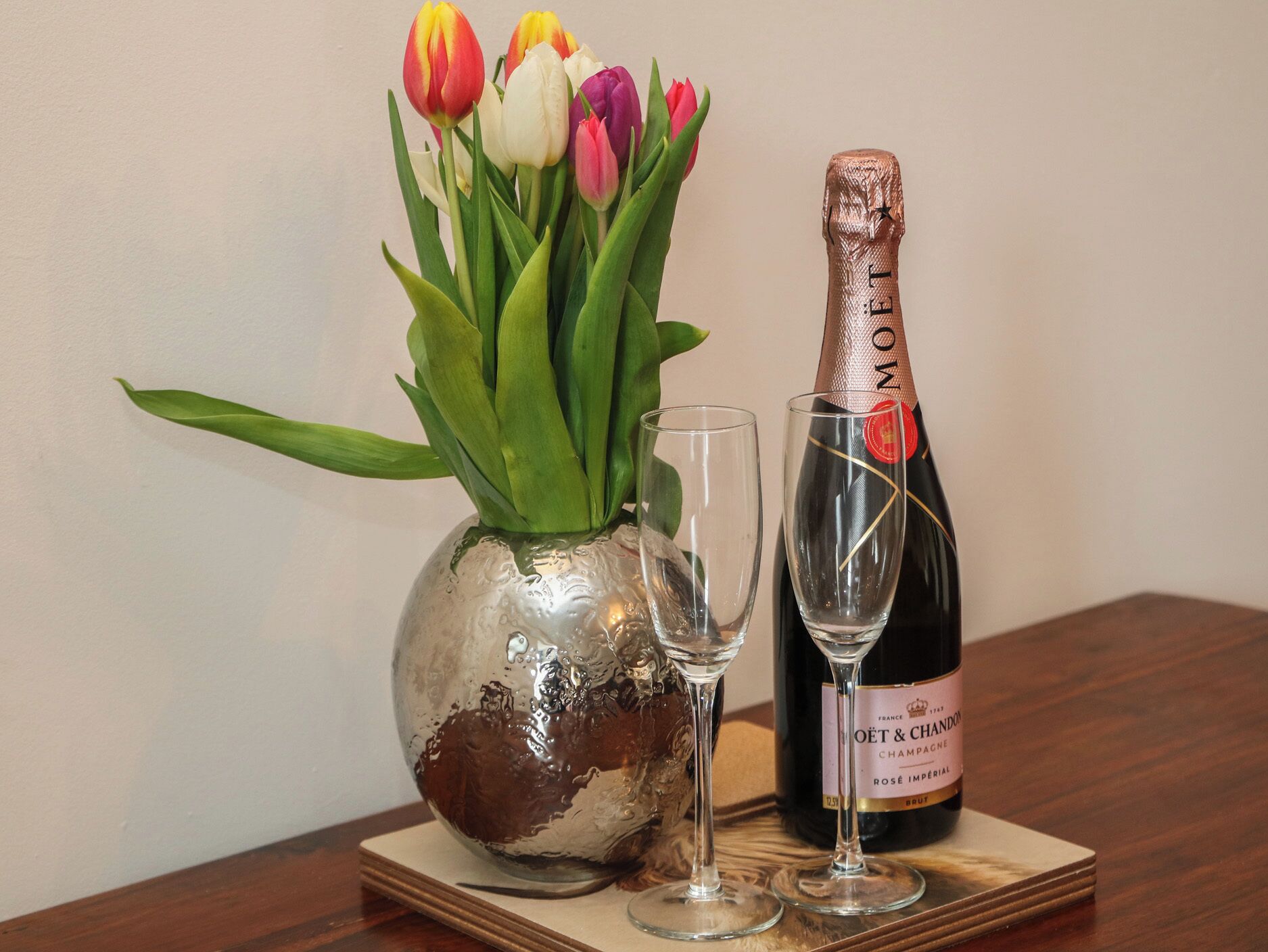 A bottle of champagne, a glass, and a vase with tulips on a wooden table.