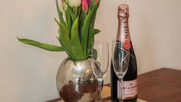 A bottle of champagne, a glass, and a vase with tulips on a wooden table.