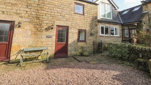 A stone building with a wooden bench, a red door, and a small garden area.