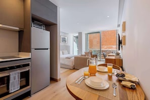 A modern kitchen with a built-in oven and a refrigerator. There is a dining area with a table set for breakfast, including plates, cutlery, and a pitcher of orange juice. - Capitalia Juarez | Central Studio + Balcony & Gym (Ciudad de México)