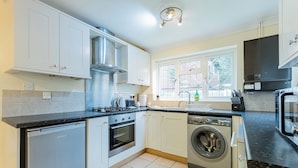 A modern kitchen with white cabinets, a dishwasher, a washing machine, and a stove.