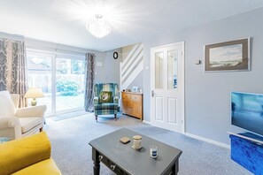 Una sala de estar con un sofá, una mesa de centro, un televisor y una escalera que lleva a otra habitación.