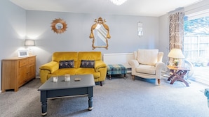 A living room with a yellow sofa, a white armchair, a wooden cabinet, and a chandelier.