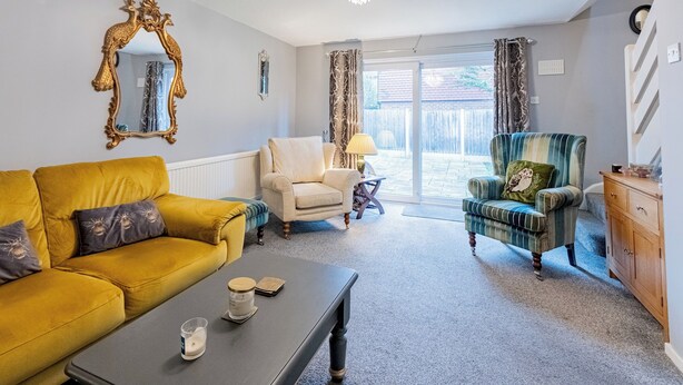 A living room with a yellow sofa, a beige armchair, a green armchair, a wooden cabinet, and a chandelier.