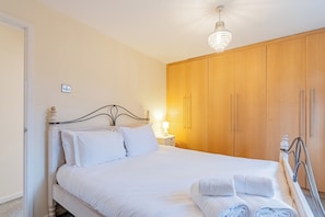 Una cama bien hecha con sábanas blancas, una lámpara de noche, un armario de madera y una araña.