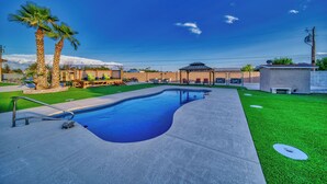 Ein Schwimmbecken mit Terrasse, Palmen und einem überdachten Sitzbereich.