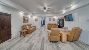Ein geräumiges Wohnzimmer mit Deckenventilator, einem an der Wand montierten Fernseher und einer Holztür.