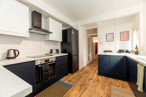 Una cocina moderna con armarios blancos, un refrigerador negro y piso de madera.