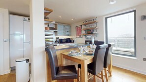 A modern kitchen with a dining area, wooden flooring, and a large window with a view. - Penthouse Sanctuary with Wraparound Balcony - Pass the Keys (London)