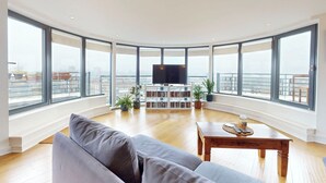 A spacious living room with a large window, a flat-screen TV, a bookshelf, and a sofa. - Penthouse Sanctuary with Wraparound Balcony - Pass the Keys (London)
