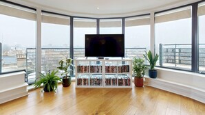 A modern living room with a large flat-screen TV, a bookshelf, and potted plants. - Penthouse Sanctuary with Wraparound Balcony - Pass the Keys (London)