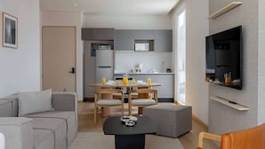 Een moderne woonkamer met een bank, een salontafel, een televisie en een eethoek met stoelen en een tafel.