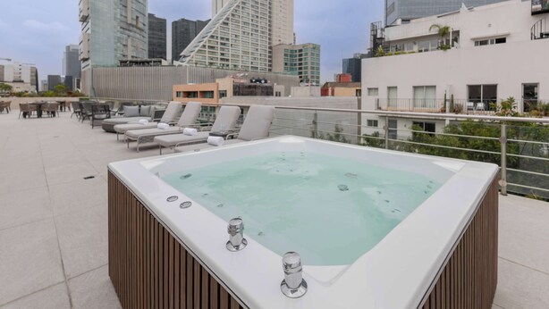 Een dakterras met een jacuzzi, lounge fauteuils en uitzicht op de stad.