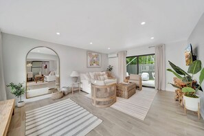 A modern living room with a white sofa, a large mirror, and a view of the outdoors. - Waterfront Retreat Studio #4🌴 20-Min Walk to the Beach Summer Deals! (Fort Lauderdale)