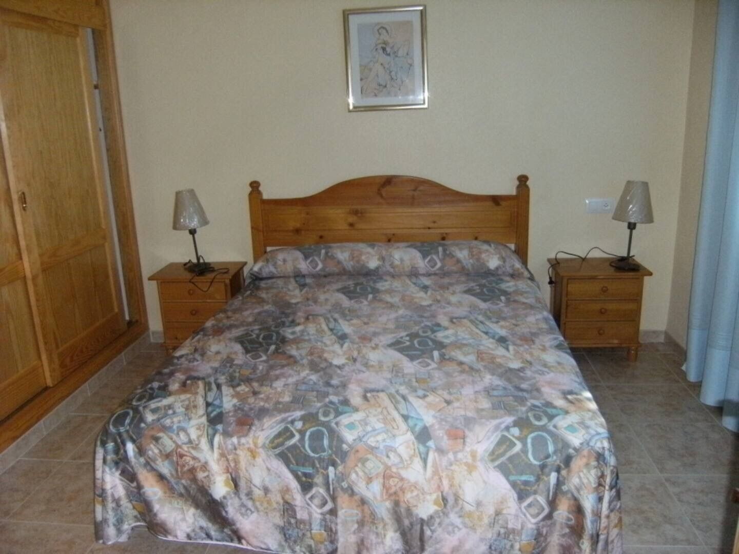 Une chambre à coucher avec un lit en bois, deux tables de chevet avec des lampes, une armoire et un tableau encadré au mur.