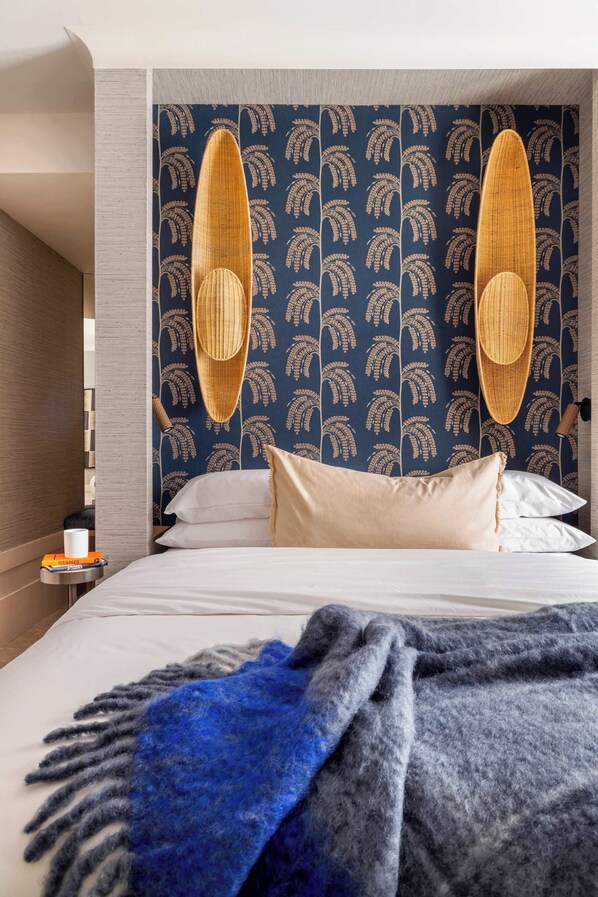 A hotel room with a bed, two wicker chairs, a patterned wallpaper, and a bedside table with a book and a cup. - Luxury Garden Suit in Recoletos (Madrid)