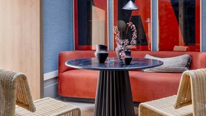 A modern lounge area with a round table, wicker chairs, a red sofa, and abstract wall art. - Luxury Garden Suit in Recoletos (Madrid)