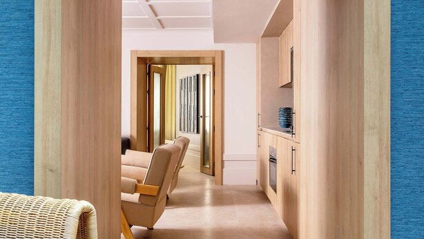 A hallway with a wooden frame, a wicker chair, and a kitchen area with cabinets and a countertop. - Luxury Garden Suit in Recoletos (Madrid)
