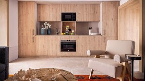 A modern kitchen with wooden cabinets, a microwave, an oven, and a seating area with a chair and a small table. - Luxury Garden Suit in Recoletos (Madrid)