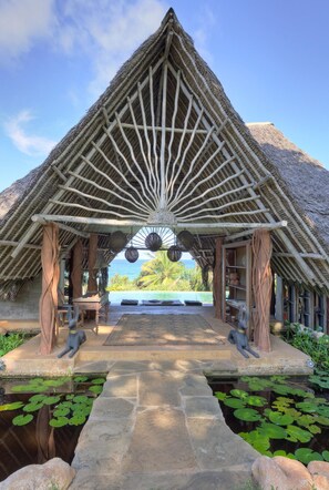 A thatched-roof pavilion with a central decorative element, a stone pathway leading to a pool with lily pads, and a view of the ocean. - VILLA SERENITY - Four Bedroom Villa, Sleeps 10 (Diani Beach)