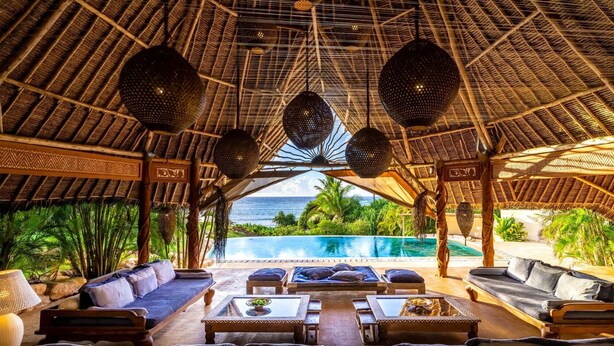 Un espace de détente doté d’un toit de chaume, avec vue sur la piscine, aménagé avec des canapés et des tables.