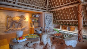 Un espace bar agrémenté d’une sculpture d’éléphant en bois, proposant une variété de boissons et une présentation attrayante de fruits.