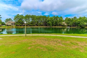 A lakeside view with a grassy area, trees, and houses in the background.