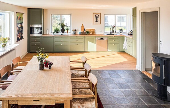A spacious kitchen with green cabinets, a dining area with a wooden table and chairs, and a fireplace.