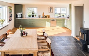 Une cuisine spacieuse avec des meubles de couleur verte, un coin repas avec une table et des chaises en bois, et une cheminée.
