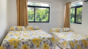 Een kamer met twee bedden, elk met bloemenbedrukking, grote ramen voorzien van gordijnen en uitzicht op groen.
