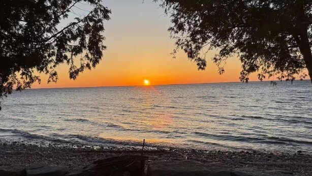 A sunset over a calm sea with a rocky shoreline and a small boat. - Sunsets on 57~perfect waterfront property in southern Door County (Luxemburg)